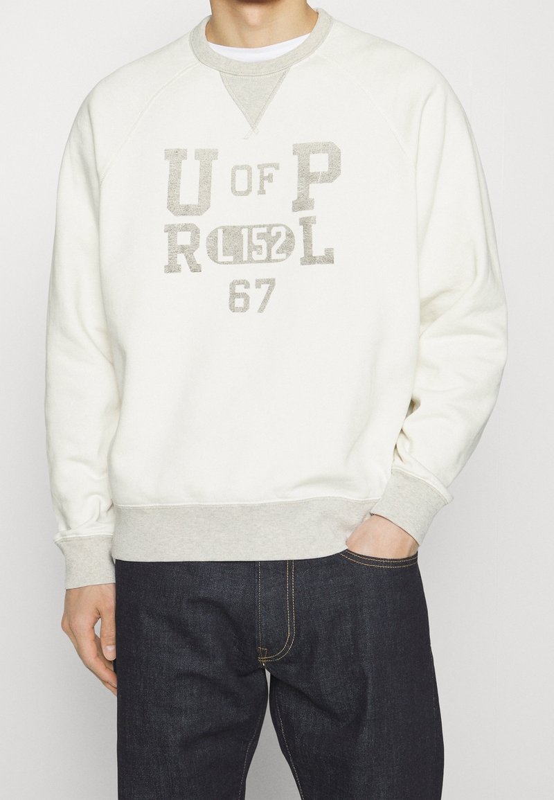 Bílá mikina s šedými detaily, která má velký potisk textu "U OF P R L 152" a "67". Hladké pružné manžety a lem, vyrobená z měkké bavlny.