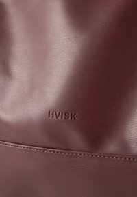 Gladka površina temno rjave usnja z drobnim šivanjem in vtisnjenim logotipom "HVISK" blizu središča.