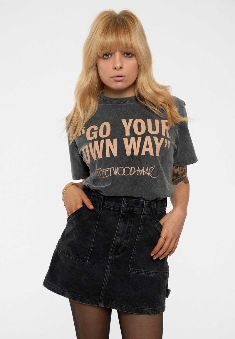 Gray oversized t-shirt featuring large peach text, “GO YOUR OWN WAY,” paired with a black denim skirt with pockets. Flat background.