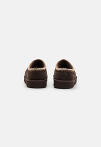 Brązowe zamszowe buty z haftowanym wykończeniem, okrągły kształt, niski profil i miękka tekstura. Widok z tyłu ukazuje gładki design z minimalistycznymi akcentami.
