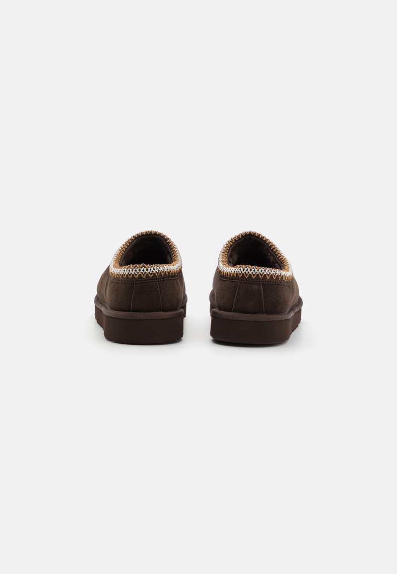 Bruine suede schoenen met gestikte randen, ronde vorm, lage profiel en een zachte textuur. De achterkant toont een strak ontwerp met minimale accenten.