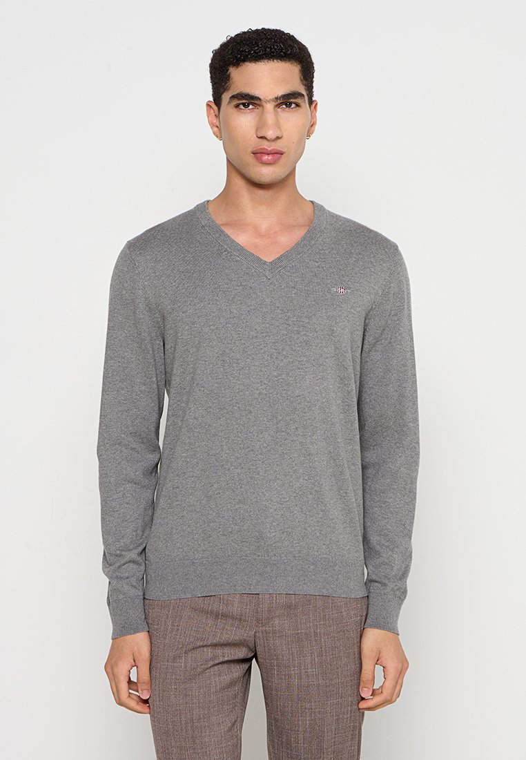 Grauer Strickpullover mit V-Ausschnitt, langen Ärmeln und kleinem gesticktem Logo auf der Brust. Leicht, mit glatter Textur und lässigem Design.