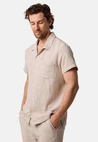 Camicia beige chiaro a maniche corte con bottoni in tessuto testurizzato, dotata di taschino sul petto e dalla vestibilità morbida.