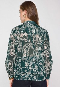 Blusa verde a fantasia con design floreali e paisley, tessuto leggero, vestibilità ampia, collo alto e polsini con bottoni.