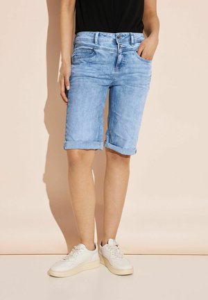 Shorts en jean bleu clair avec des ourlets retroussés, cinq poches et une fermeture à bouton. Portés avec des baskets blanches sur un fond pâle.