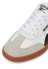 Tenis alb din piele cu accente din suede gri, logo negru și talpă din cauciuc texturată. Prezintă șireturi albe și detalii cusute.