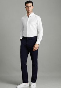 Cămașă albă cu guler, dotată cu un buzunar pe piept, asociată cu pantaloni în nuanțe închise de navy și adidași albi. Material fin cu o croială ajustată.