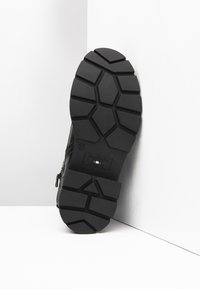 Sort gummisko sål med en tekstureret, mønstret grip med hexagonale slidbanedetaljer og et logo. Lynlåsdesign på overdelen synlig.