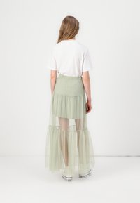 Jupe maxi en tulle vert clair avec un design en étages, une taille élastique et un ourlet superposé, associée à un t-shirt blanc et des baskets.