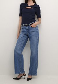 Námorní ribovaný top s krátkým rukávem a krouceným detailem a čtvercovým výstřihem, doplněný světle modrými vysokými širokými kalhotami a černými podpatky.