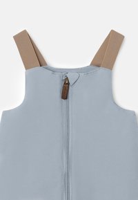 Lys blå uten ermer plagg med beige stropper, og en sentral glidelås med en brun aksent. Glatt tekstur og ren design.