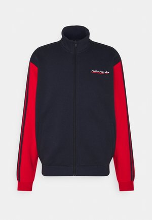 Marineblau und rotes Zip-Up-Jacke mit langen Ärmeln, featuring drei schwarze Streifen an jedem Arm und einem gestickten Logo auf der Brust.