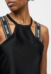 Γυναίκα που φοράει μαύρο τοπ με τιράντες Just Cavalli μαύρες και λευκές με λογότυπο, μπροστά σε ουδέτερο φόντο.