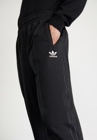 Svarta joggerbyxor i mjukt tyg med elastisk midjeband, sidoficka och tre ränder längs benen. Adidas-logotyp framtill.