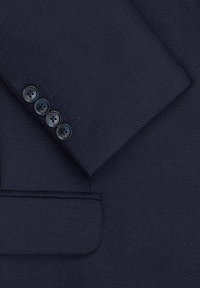 Navy blazer z tkaniny o teksturowanym splocie, z klapami w szpic i czterema ciemnymi guzikami na mankietach. Widoczne subtelne detale w szyciu.