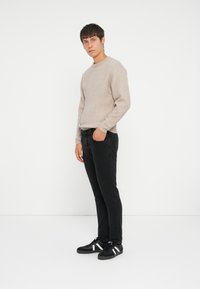 Beige knit sweater, black jeans, and black sneakers with white stripes. The sweater features ribbed cuffs and hem, smooth texture.