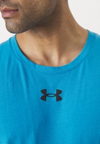 Lys blå bomullsinglet med en svart Under Armour-logo på brystet, med en crew neck-design og glatt tekstur.
