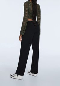 Olive green crochet long-sleeve crop top with a round neckline, paired with black wide-leg pants and white sneakers with black accents.