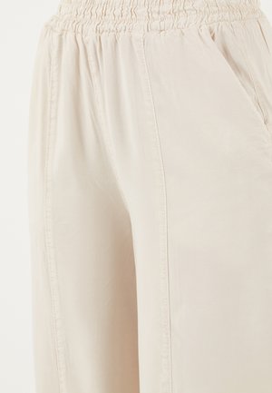 Heledad beežid püksid elastse vöökohaga ja ees taskutega, valmistatud pehmest ja kergest kangast.