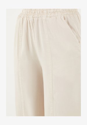 Heledad beežid püksid elastse vöökohaga ja ees taskutega, valmistatud pehmest ja kergest kangast.