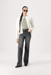 Cardigan branco tricotado, blusa verde texturizada, jeans cinza escuro flared, sapatos pretos, óculos de sol. Penteado trançado. Estilo simples e moderno.