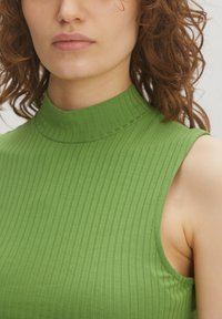 Groen geribbeld mouwloos topje met een hoge kraag en een strakke pasvorm, dat een gladde textuur en verticale lijnen toont.