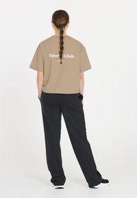 Beige lyhythihainen t-paita, jonka selässä lukee "Urheiluseura"; yhdistetty mustiin rentoihin housuihin ja lenkkareihin. Silkkinen pinta.