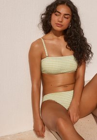 Zöld kockás bikini szett, négyzet alakú dekoltázzsal és vékony, áll adjustable pántokkal. Az anyag texturált megjelenésű, fodros részletekkel.