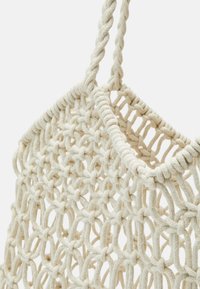 Krémová tkaná taška vyrobená z hustého, strukturovaného lana. Má síťkový design s pletenými ušima a otevřeným vrškem.