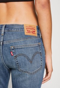 Siniset farkut, joissa on nahkainen Levi Strauss & Co. -merkki, näkyvät saumat ja erottuva punainen etiketti takataskussa.