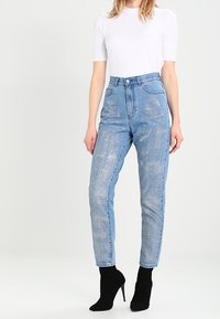 Dámské modré džíny s vysokým pasem a vybledlým designem, s pěti kapsami a rovnými nohavicemi, doplněné černými botami na podpatku k kotníkům.