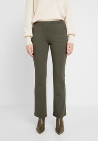 Olijfgroene broek met een rechte pasvorm en een gladde textuur, gecombineerd met een crème trui en puntige bruine enkellaarsjes.