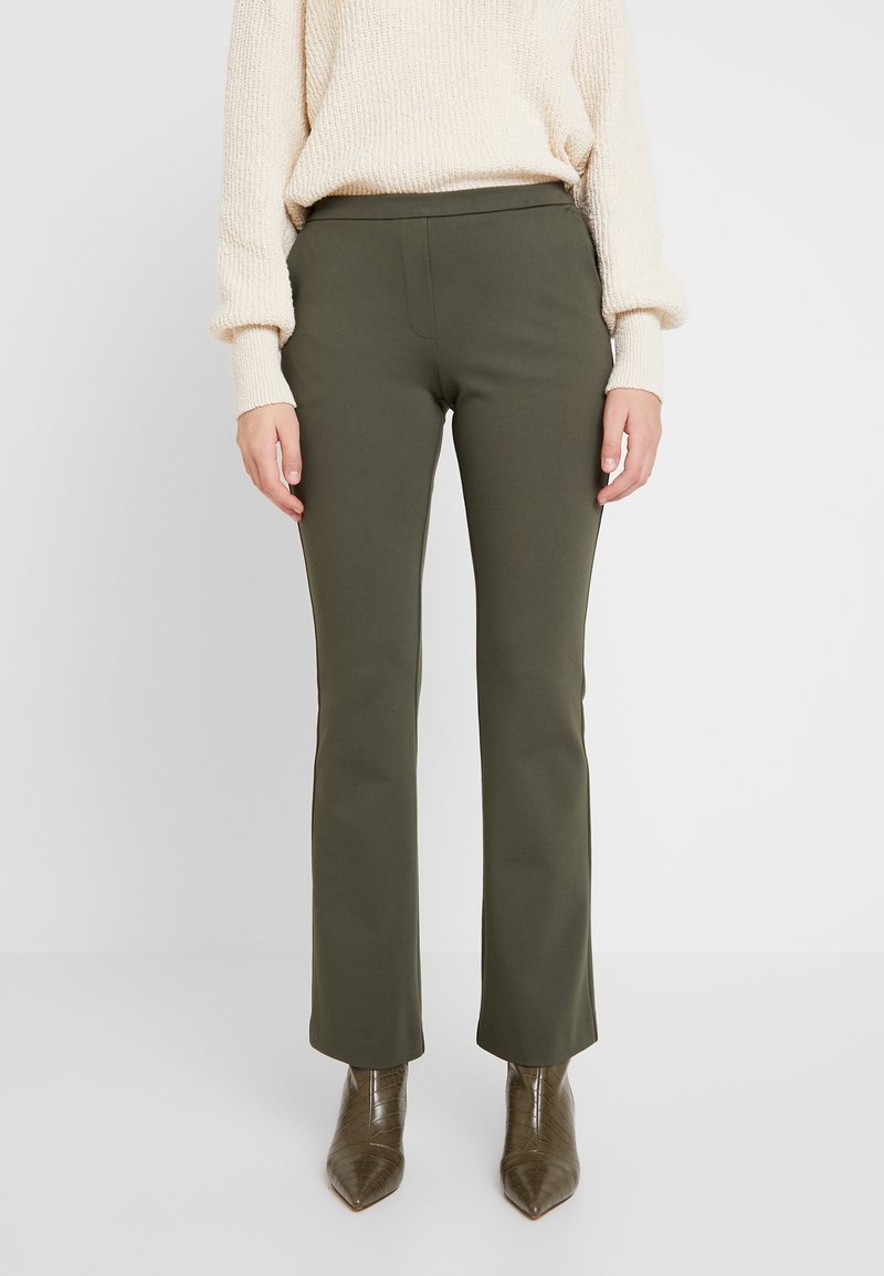 Olijfgroene broek met een rechte pasvorm en een gladde textuur, gecombineerd met een crème trui en puntige bruine enkellaarsjes.
