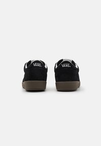 Crne nubuk Vans tenisice s smešnim gumiranim đonom. Bijeli logo na peti, podstavljeni ovratnik i minimalistički dizajn.