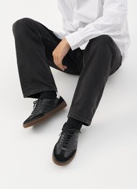 Melnas sporta kurpes ar gludu un teksturētu virsu, apgādātas ar gumijas zoli un tumšiem auklām. Saskaņotas ar melniem džinsiem un baltu svītrainu krekls.