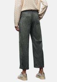 Green, soft velvet trousers with a wide fit, patch pockets, and contrast stitching. Paired with a textured cream sweater and light sneakers.