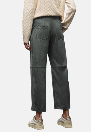 Pantalon en velours vert, doux, à coupe large, avec poches appliquées et coutures contrastées. Associé à un pull texturé crème et des baskets claires.
