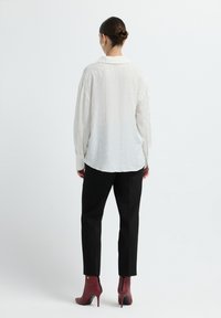 White textured shirt with a collar, loose fit, and buttoned cuffs, paired with black trousers and burgundy high-heeled ankle boots.
