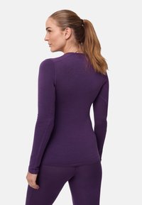 Lila langärmeliges Oberteil aus glattem, elastischem Material, mit figurbetontem Schnitt und Nahtdetails entlang der Schultern und Seiten.