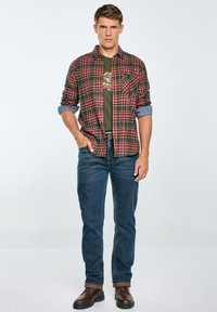 Cămașă în carouri roșii și negre purtată peste un tricou grafic verde, împreună cu blugi albaștri și cizme maronii cu șireturi. Smith oferă un aspect casual.