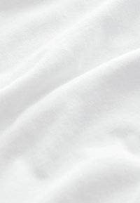 Witte katoenen stof met een gladde textuur, met subtiele plooien en rimpels, die het licht in zachte, gedempte tonen weerkaatst.