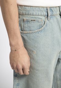 Silver chain bracelet with a small star accent, worn on a hand next to light blue denim jeans with a faded, distressed texture.