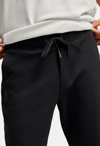 Sorte sweatpants med snøre i taljen, lavet af en glat bomuldsblanding med et diskret logo på siden. Struktureret stoffinish.