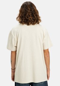 Béžové bavlněné tričko s volným, oversized střihem, krátkými rukávy a kulatým výstřihem. Zobrazuje zadní pohled s hladkou texturou.