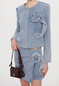 Jasnoniebieska kurtka jeansowa z kwiatową aplikacją, złotymi guzikami oraz dopasowaną spódnicą o marszczonym kroju. Do zestawu dołączona jest brązowa błyszcząca torebka.