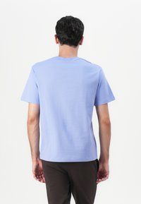Helles blaues T-Shirt mit kurzen Ärmeln aus weichem Stoff, mit Rundhalsausschnitt, glatter Textur und minimalen Details, kombiniert mit dunkelbraunen Hosen.