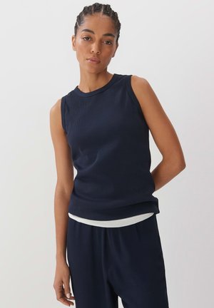 Marineblaues ärmelloses Top mit gerippter Textur, rundem Halsausschnitt und figurbetonter Silhouette. Über einem helleren Shirt am Saum geschichtet.