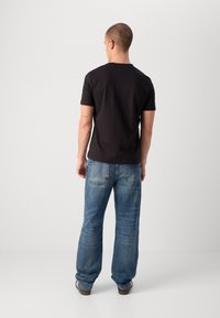 Tricou negru cu mânecă scurtă asociat cu blugi denim deschiși, cu o croială lejeră. Tricoul are un guler rotund; blugii au buzunare la spate.