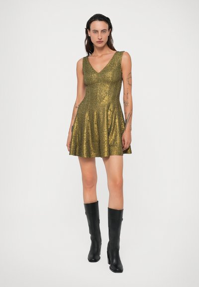 Aukso blizgučiais padengta suknelė su V formos iškirpte, platėjanti sijoną ir prigludusia liemene. Dėvima su juodais iki kelių batais, turinčiais lygią tekstūrą.