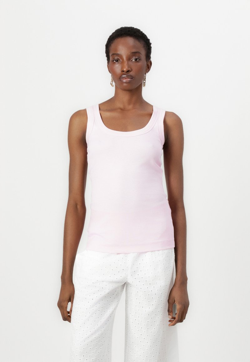 Lichtroze tanktop met een ronde hals en brede schouderbanden, gemaakt van een gladde, rekbare stof. Gepaard met witte broeken van broderie anglaise.